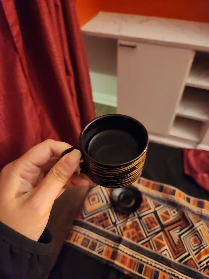 A black-and-gold tea cup held over a woven Filipino runner