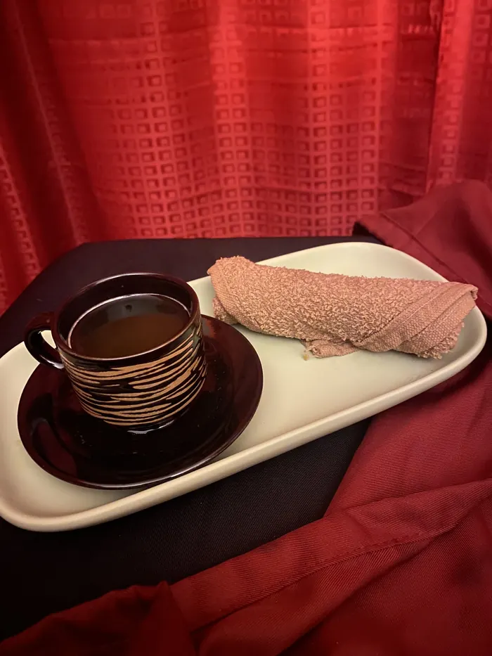 Tea in a black-and-gold cup on a tray with a rolled warm towel